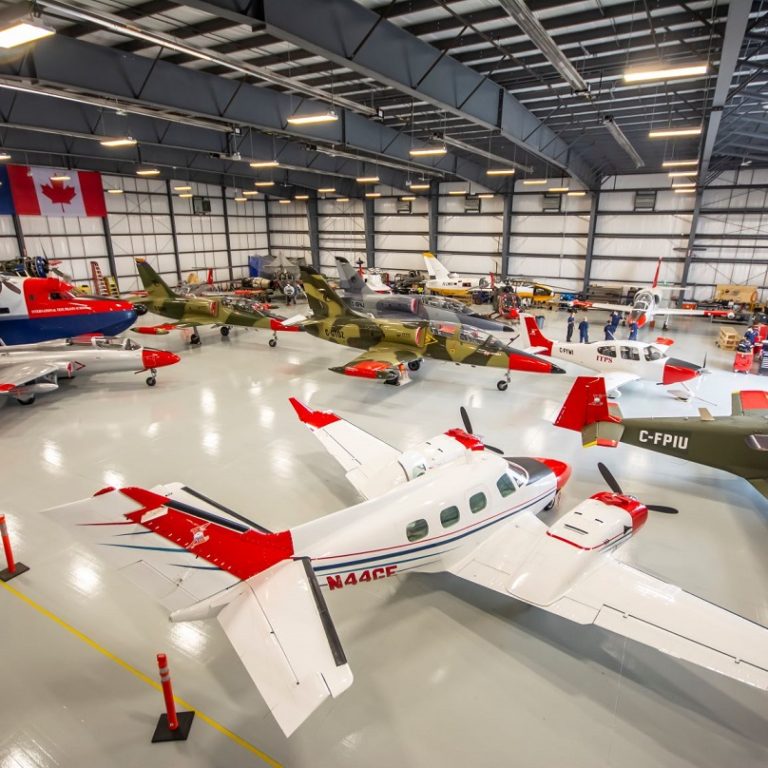 The inside of a hangar full of red tailed and white planes, Canadian flag hung in background on wall with ITPS logo