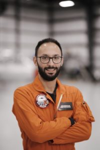 Joao Falcao in orange flight suit in the hangar.