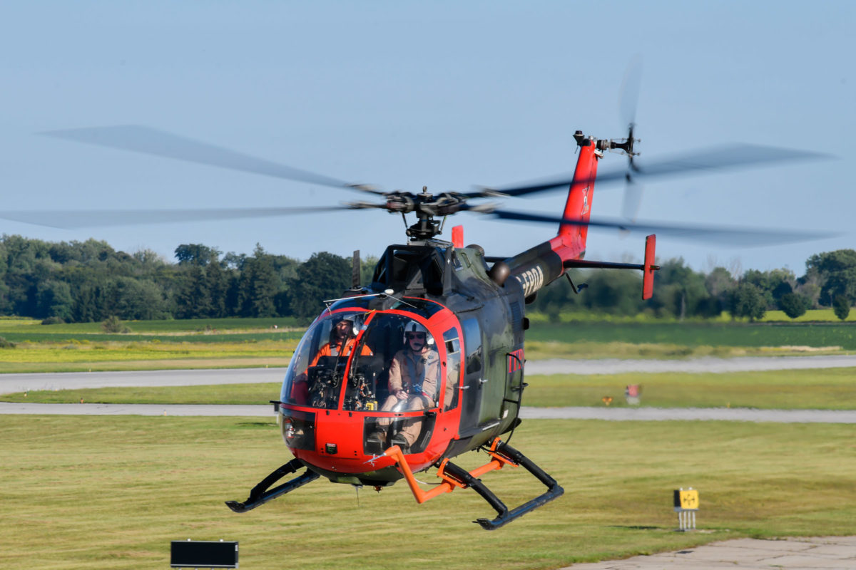 Green and red MBB Bo105 helicopter landing on tarmac.