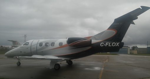 Black and white Embraer Phenom 100 aircraft on tarmac in rainy weather