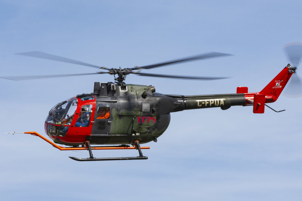Green and red MBB Bo105 helicopter with blue sky