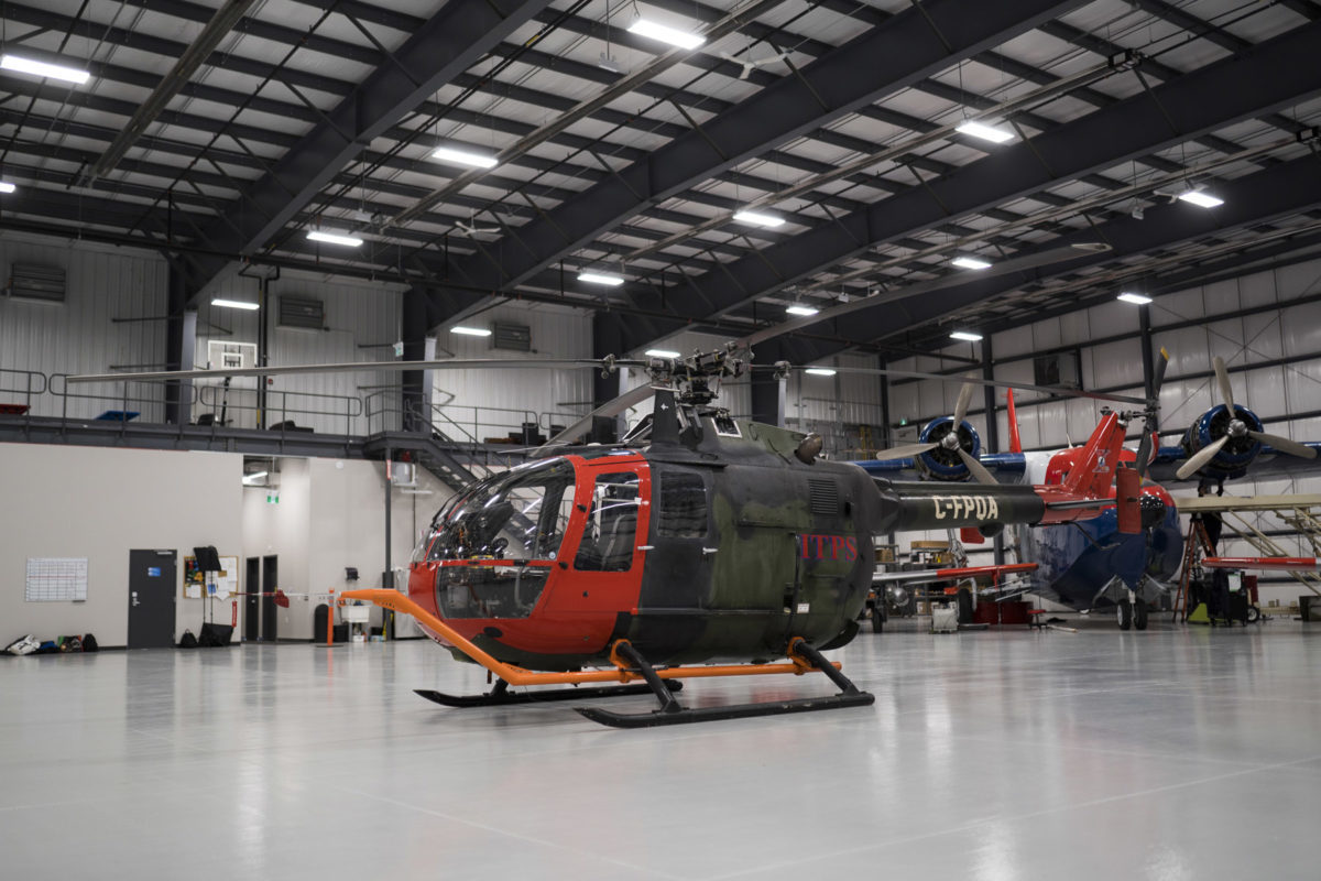 Green and red Bo-105M helicopter in hangar with attached tug