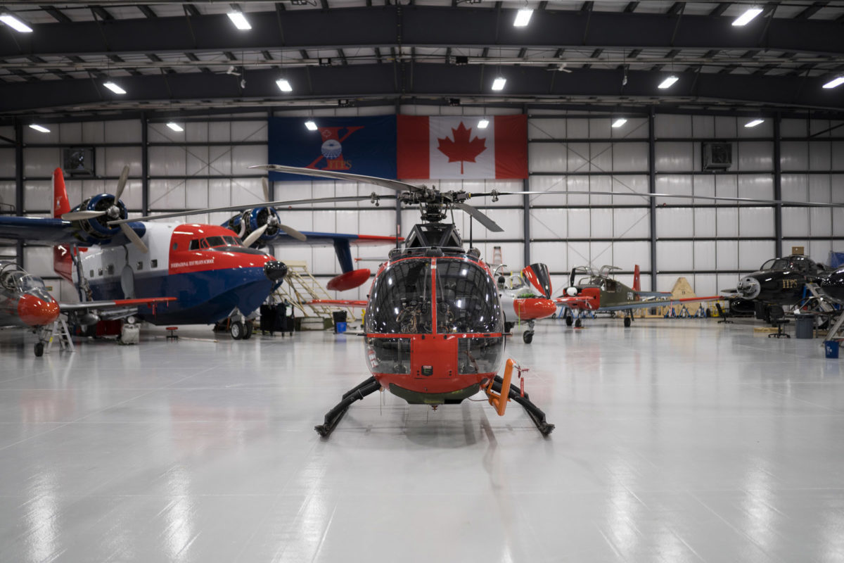 Green and red Bo-105M helicopter in hangar with HU-16 albatross in the background