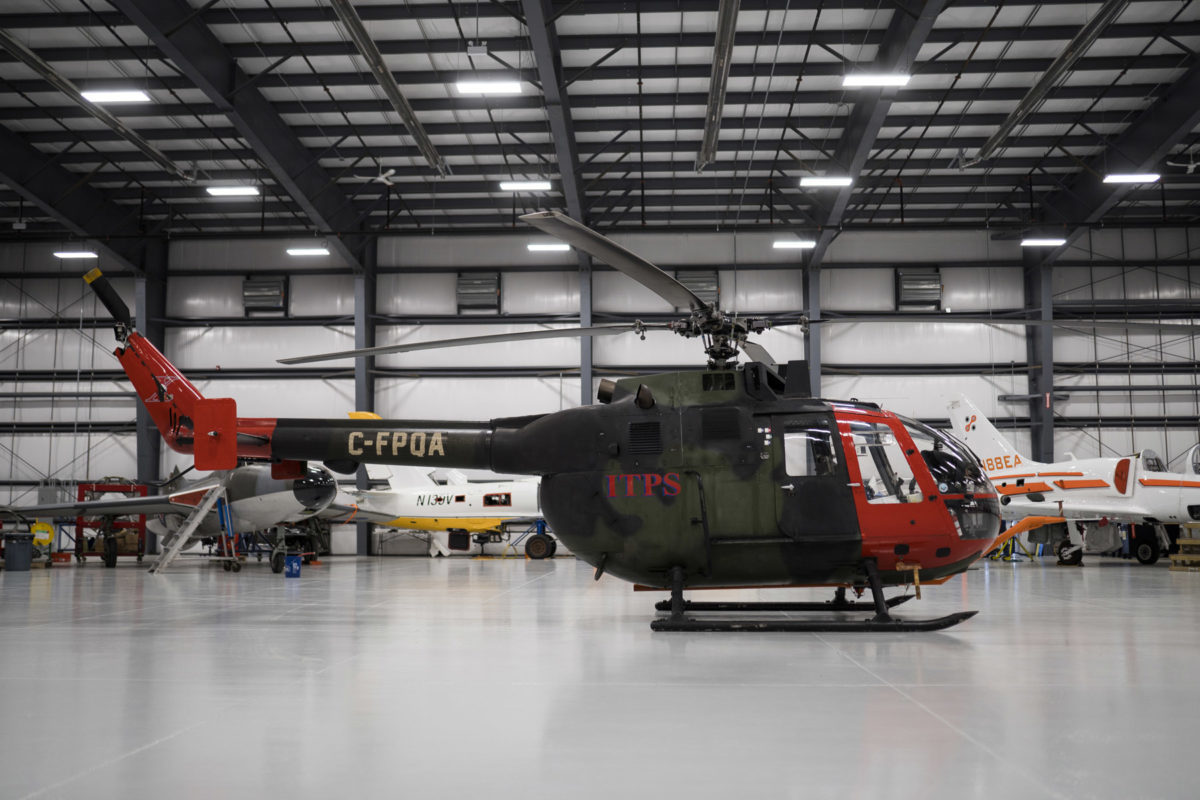 Green and red Bo-105M helicopter in hangar side
