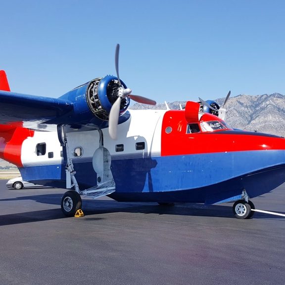 White, red and blue ITPS HU-16 Sea Plane parked on tarmac in front of mountains
