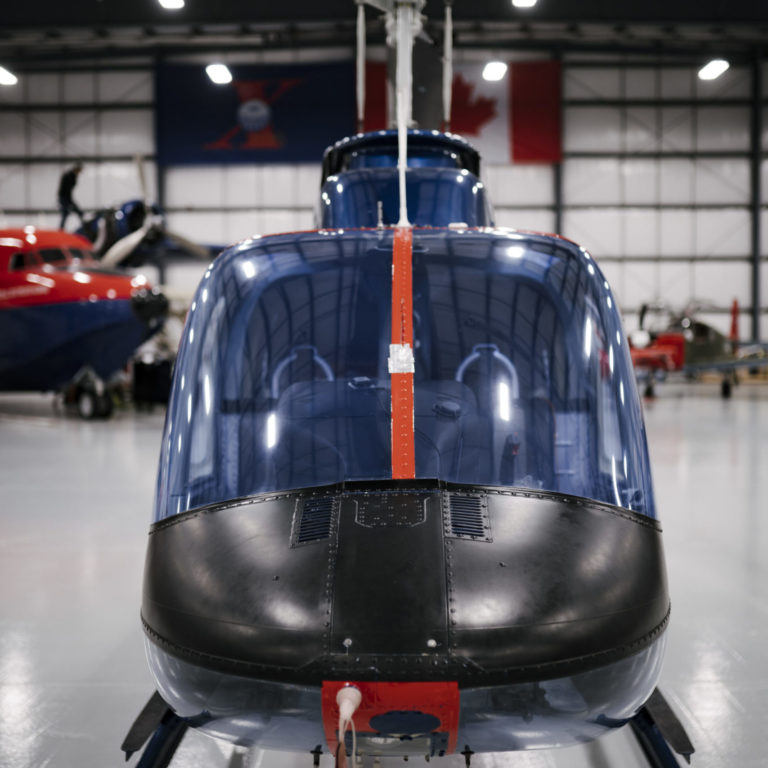 front of the cockpit tinted blue windows are the prominent feature of an ITPS Bell 206 parked in the hangar.