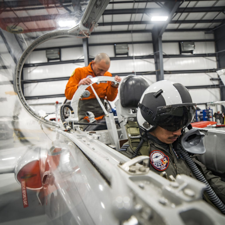 ITPS students and teachers practice onboarding on a silver, parked plane in the hangar.