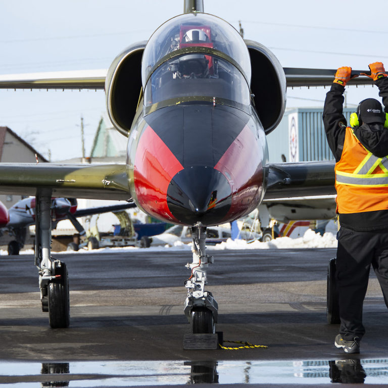 Ground crew on the air apron handle a black nosed, red paneled ITTC L-39.