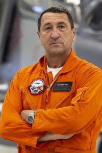 Constantin Stan in orange flight suit with arms crossed.