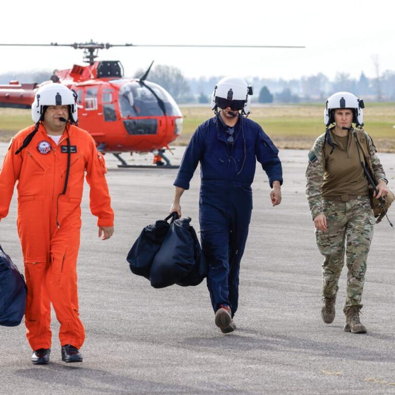 rotary wing instructor walking with two rotary wing masters students with helicopter in the background