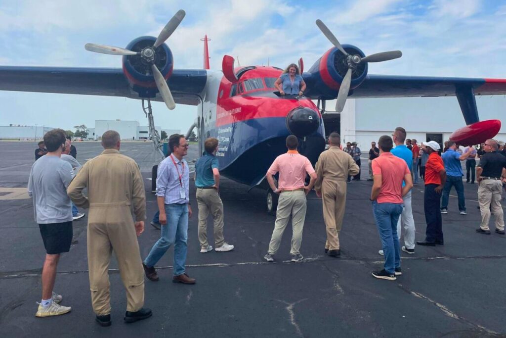 3 Group of people looking at woman peaking out of nose of HU-16 on ramp