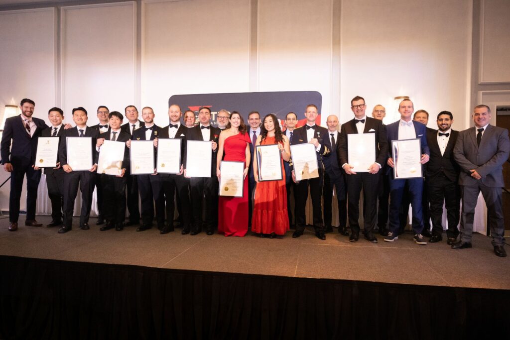 ITPS graduates stand together holding plaques with instructors