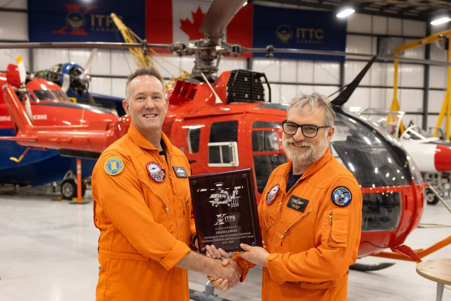 Dave Lohse, ITPS CEO holding plaque, shaking hands with Adam Lowes in hangar