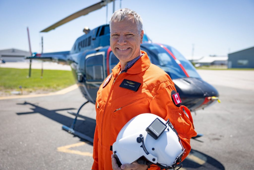 Peter Scheidler with orange flight suit in front of ITPS Bell 206 helicopter
