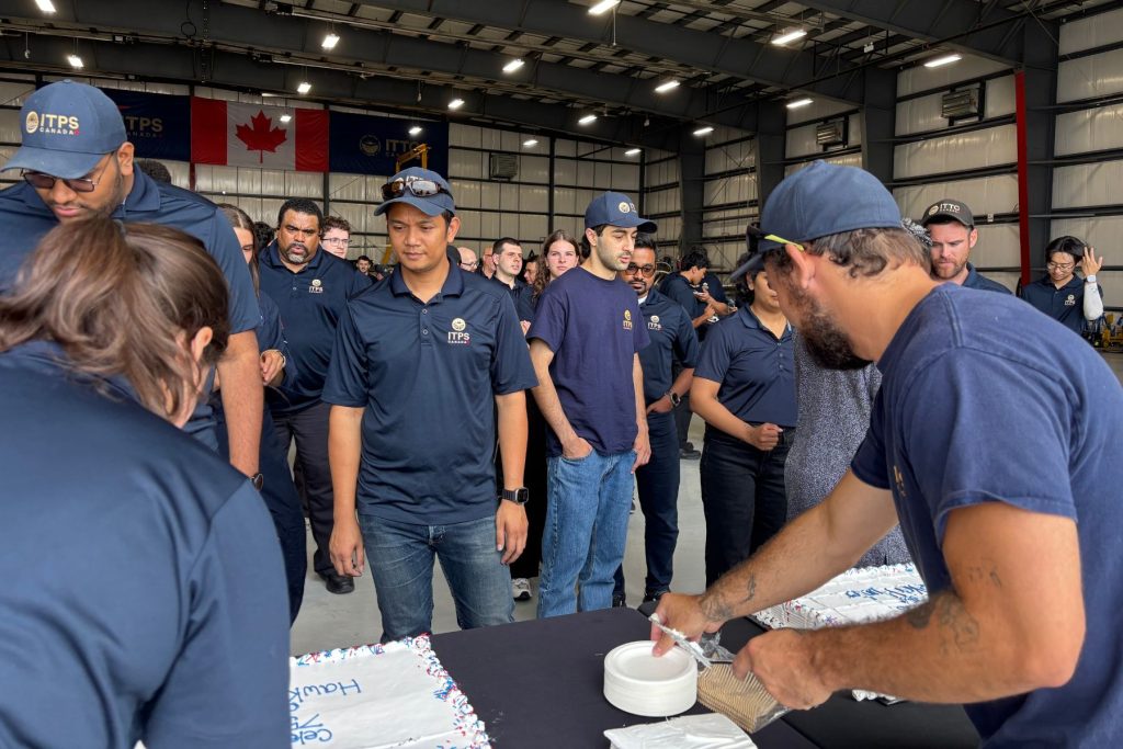 9 ITPS staff and instructors getting cake in ITPS hangar